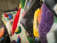 Detailaufnahme einer Boulderwand mit verschiedenfarbigen Klettervolumen und Griffen in Gelb, Rot, Lila und Orange, im Hintergrund weitere bunt bestückte Wandflächen.